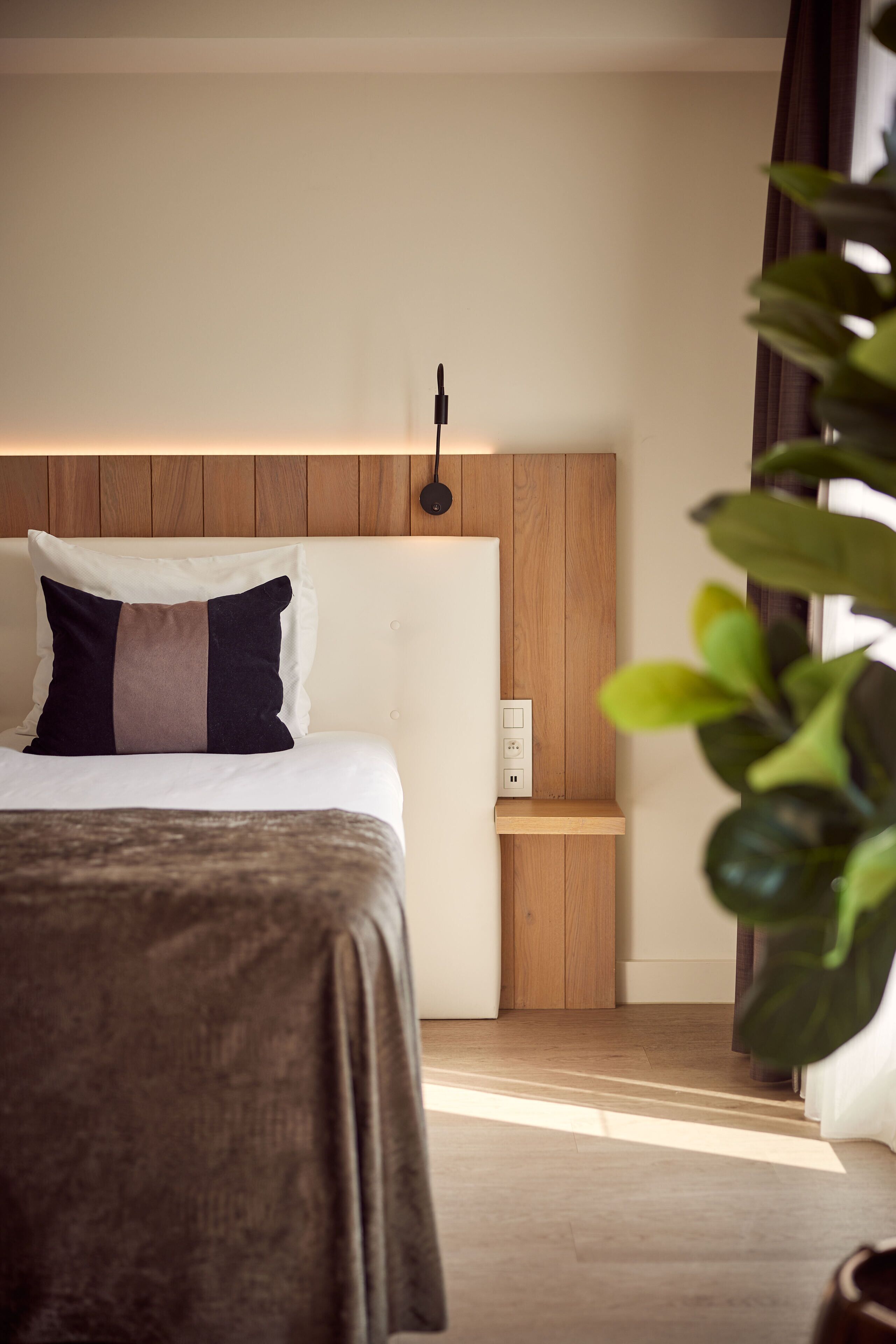 Una habitación de hotel con cama, mesita de noche, luz en la pared y una planta en maceta.