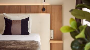 Una habitación de hotel con cama, mesita de noche, luz en la pared y una planta en maceta.