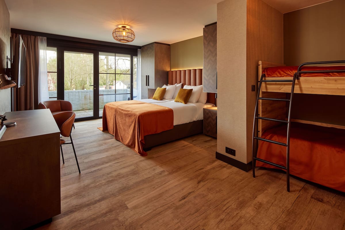 Une chambre d’hôtel avec un lit, un bureau, une chaise, un lit superposé et une grande fenêtre.