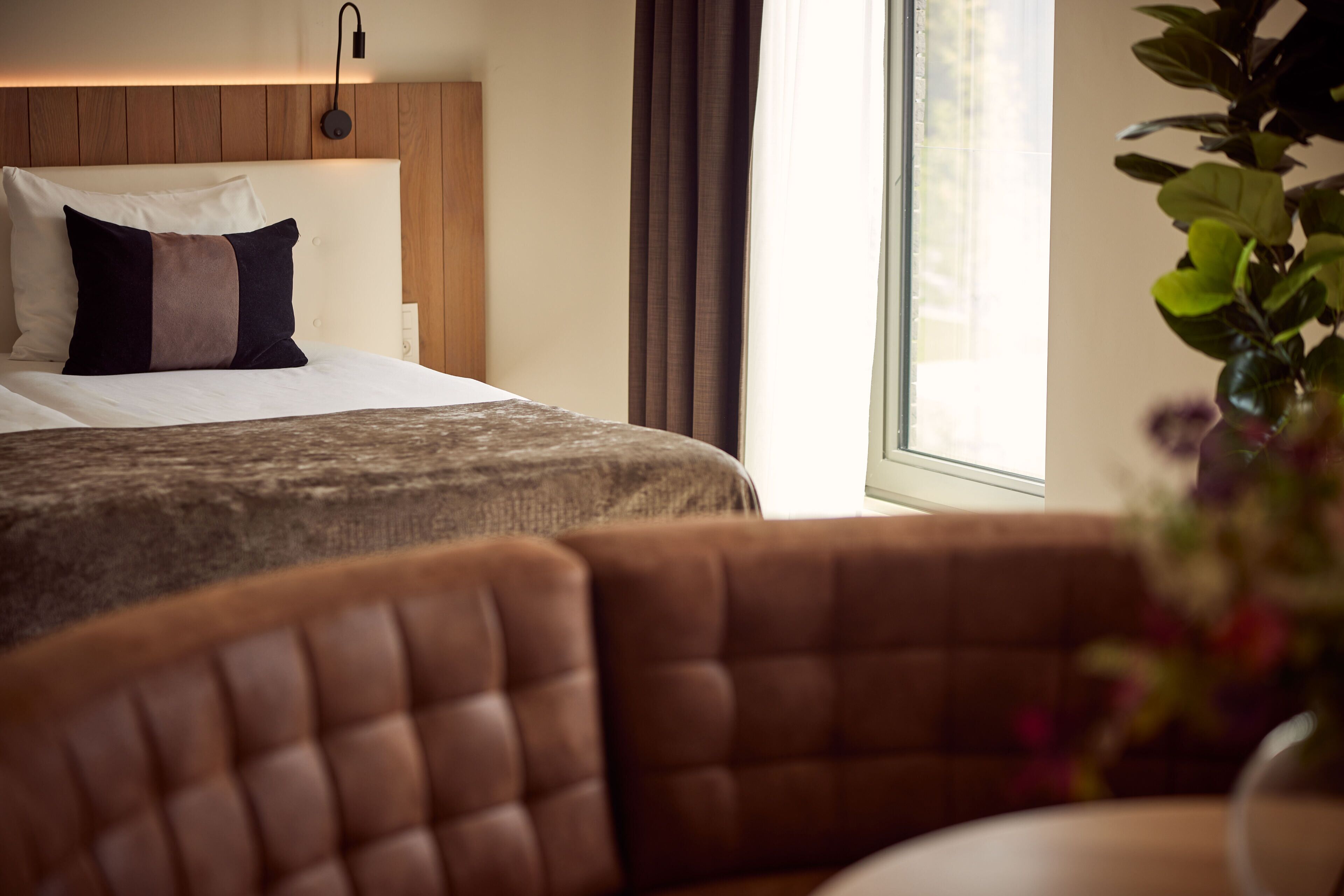 Een hotelkamer met een bed, een hoofdeinde, een raam en een bruine lederen fauteuil.