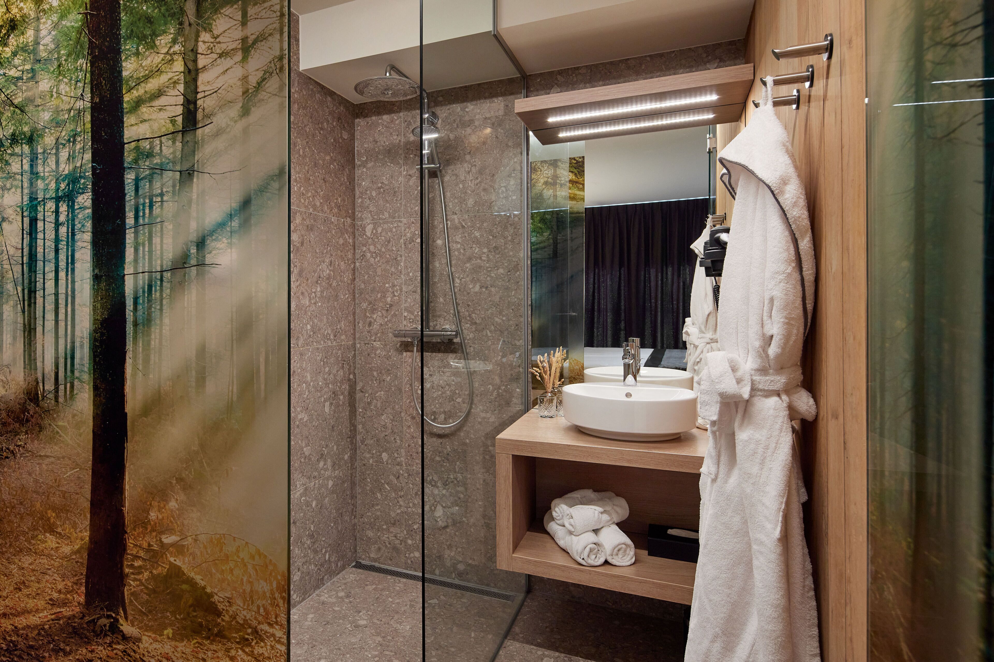 A modern bathroom with a glass-enclosed shower, a wooden vanity with a sink, and a robe hanging on a rack.