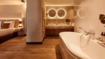 Un baño de hotel moderno con una bañera grande, dos lavamanos y un espejo con luces circulares.