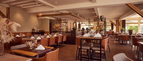 Un restaurante espacioso con techos altos, vigas a la vista y diversas opciones de asientos, incluyendo mesas y cabinas.