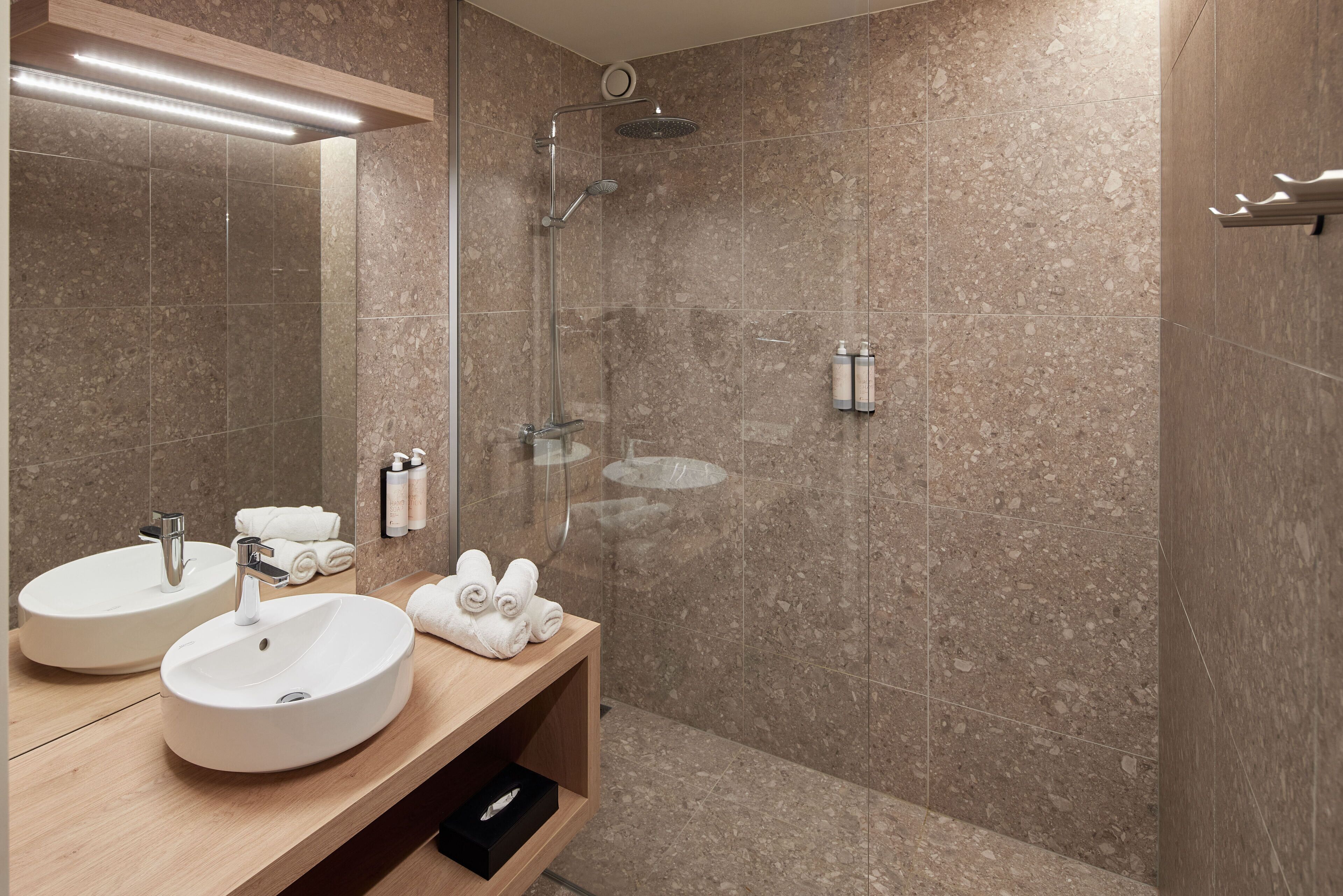A modern bathroom with two sinks, a shower, and a wooden vanity.