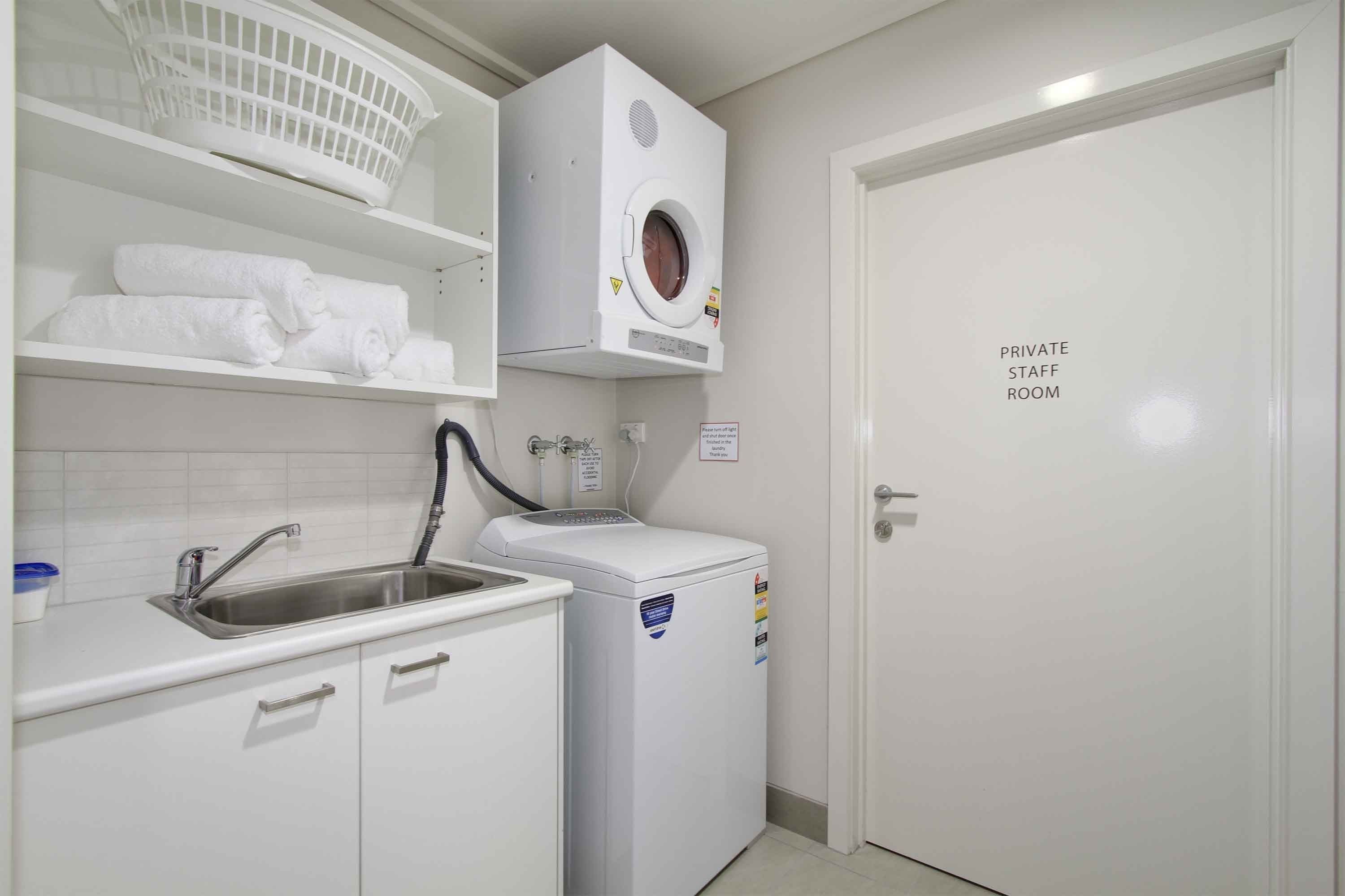 A private staff room with a washing machine, a sink, and neatly folded towels on shelves.