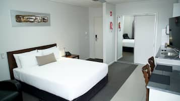 A hotel room with a bed, a desk, a chair, a ceiling fan, and a bathroom visible through a door.