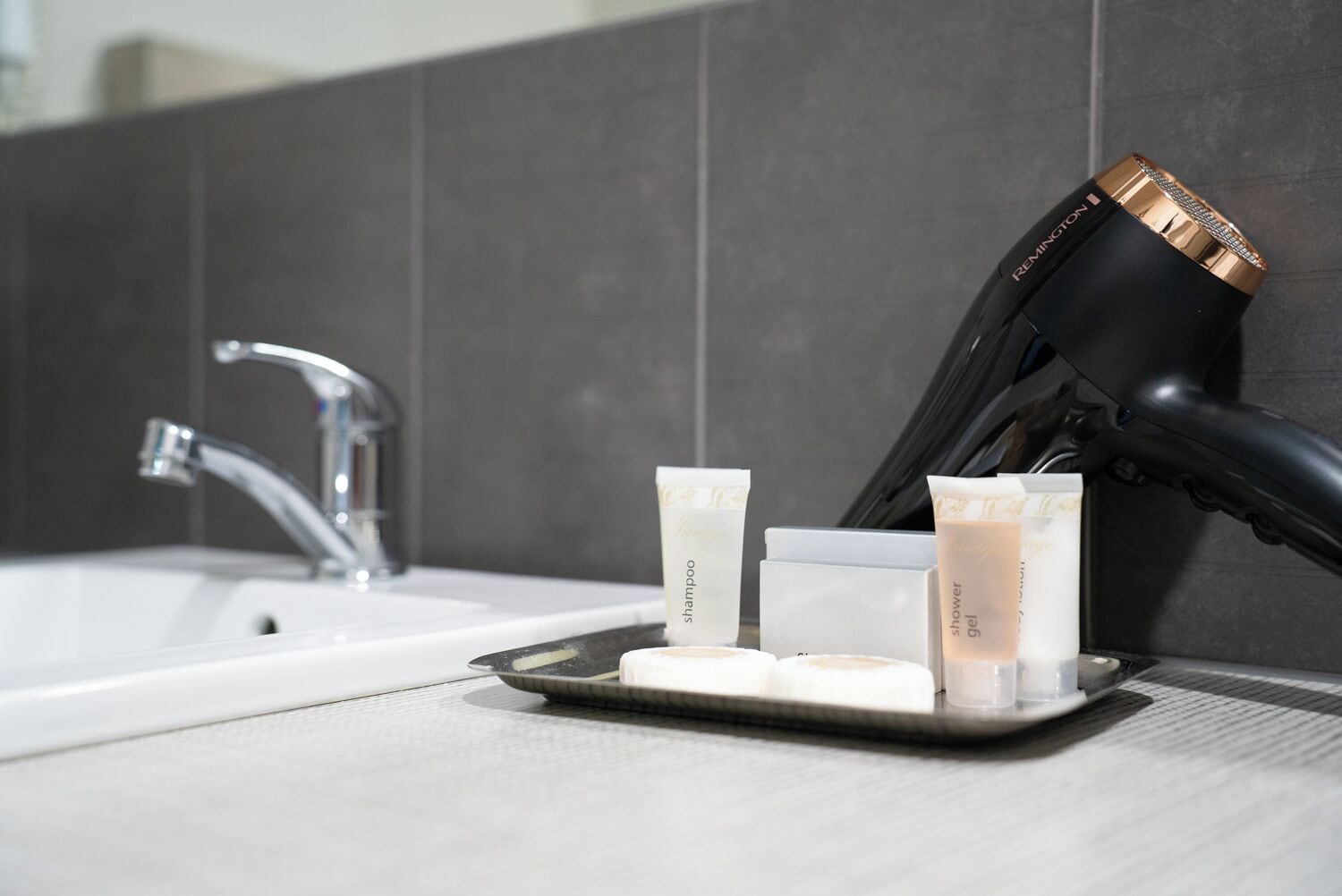 A bathroom with a white sink, a hairdryer, and three toiletries on a tray.