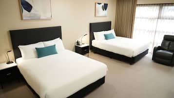 A hotel room with two beds, a nightstand, a lamp, and a chair.