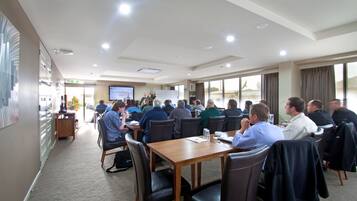 A conference room with a large table and chairs, a screen at the front, and a view of the outdoors through large windows.