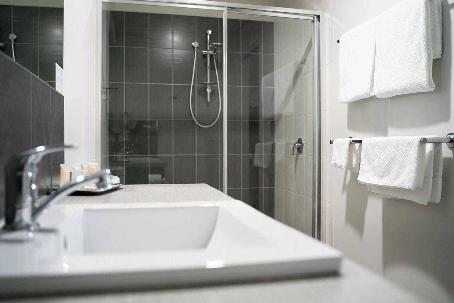 A modern bathroom with a glass-enclosed shower, a white sink, and multiple white towels on a rack.