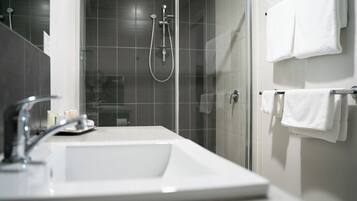 A modern bathroom with a glass-enclosed shower, a white sink, and multiple white towels on a rack.