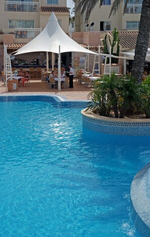 Une piscine dont le bord est revêtu de carrelage, entourée d’un espace de détente extérieur avec des sièges et des parasols.