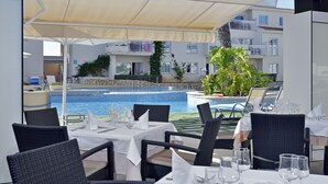 A poolside dining area with tables set for two, overlooking a swimming pool. - Hotel Isla de Cabrera (Ses Salines)