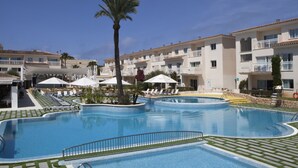 A swimming pool with lounge chairs and umbrellas, surrounded by multi-story buildings with balconies. - Hotel Isla de Cabrera (Ses Salines)