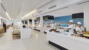 A modern restaurant with white and blue decor, multiple serving stations, and a clean, spacious layout. - Hotel Isla de Cabrera (Ses Salines)