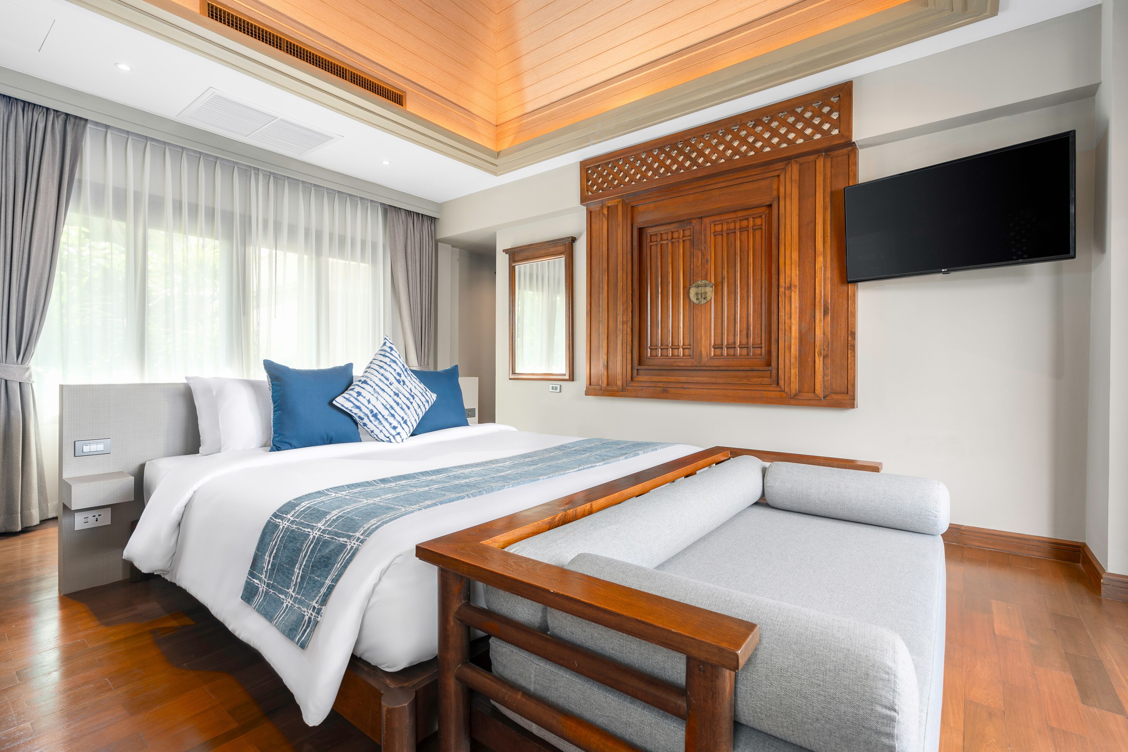 Een hotelkamer met een groot bed, een aan de muur bevestigde televisie en een houten hoofdeinde.