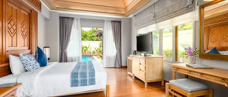 A bedroom with a bed, wooden desk, TV, and a view of a swimming pool.