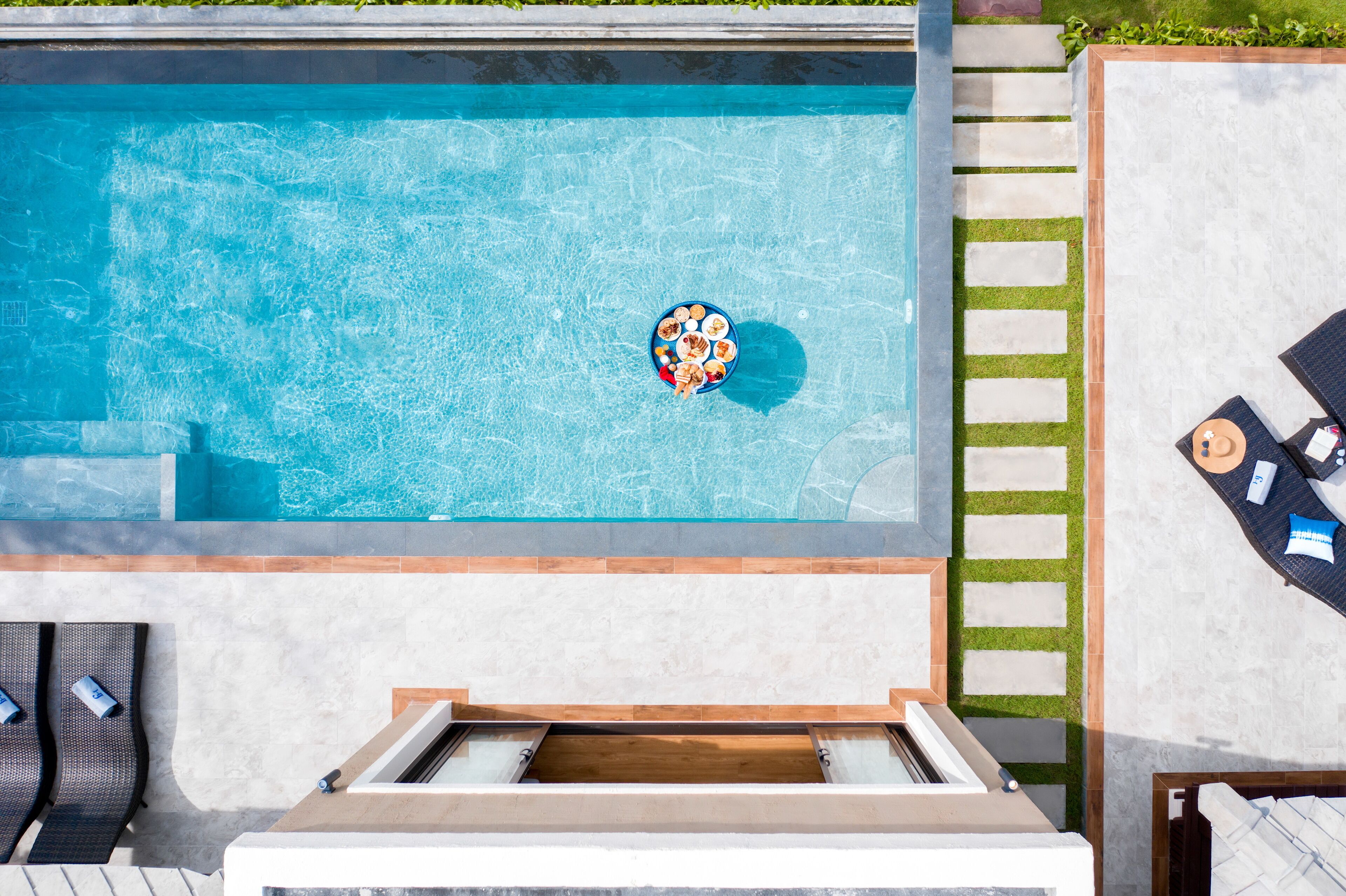 A rooftop pool with a floating bar, lounge chairs, and a stone pathway.