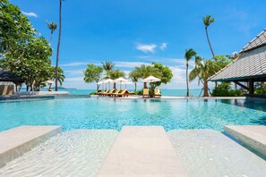 A clear pool with lounge chairs and umbrellas, surrounded by palm trees and a view of the ocean. - Fair House Villas & Spa (Koh Samui)