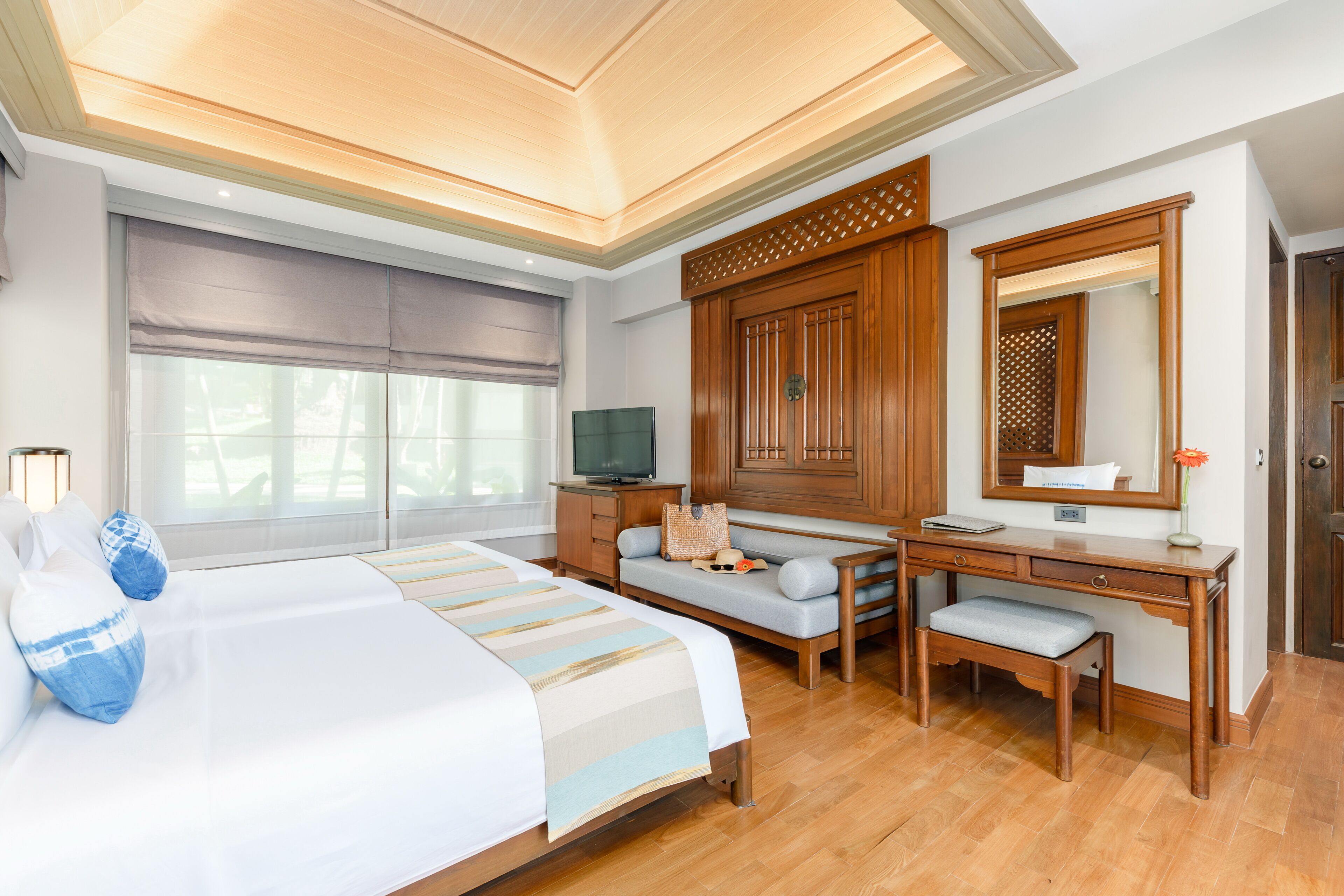 A hotel room with a large bed, a desk, a chair, a television, and a wardrobe.