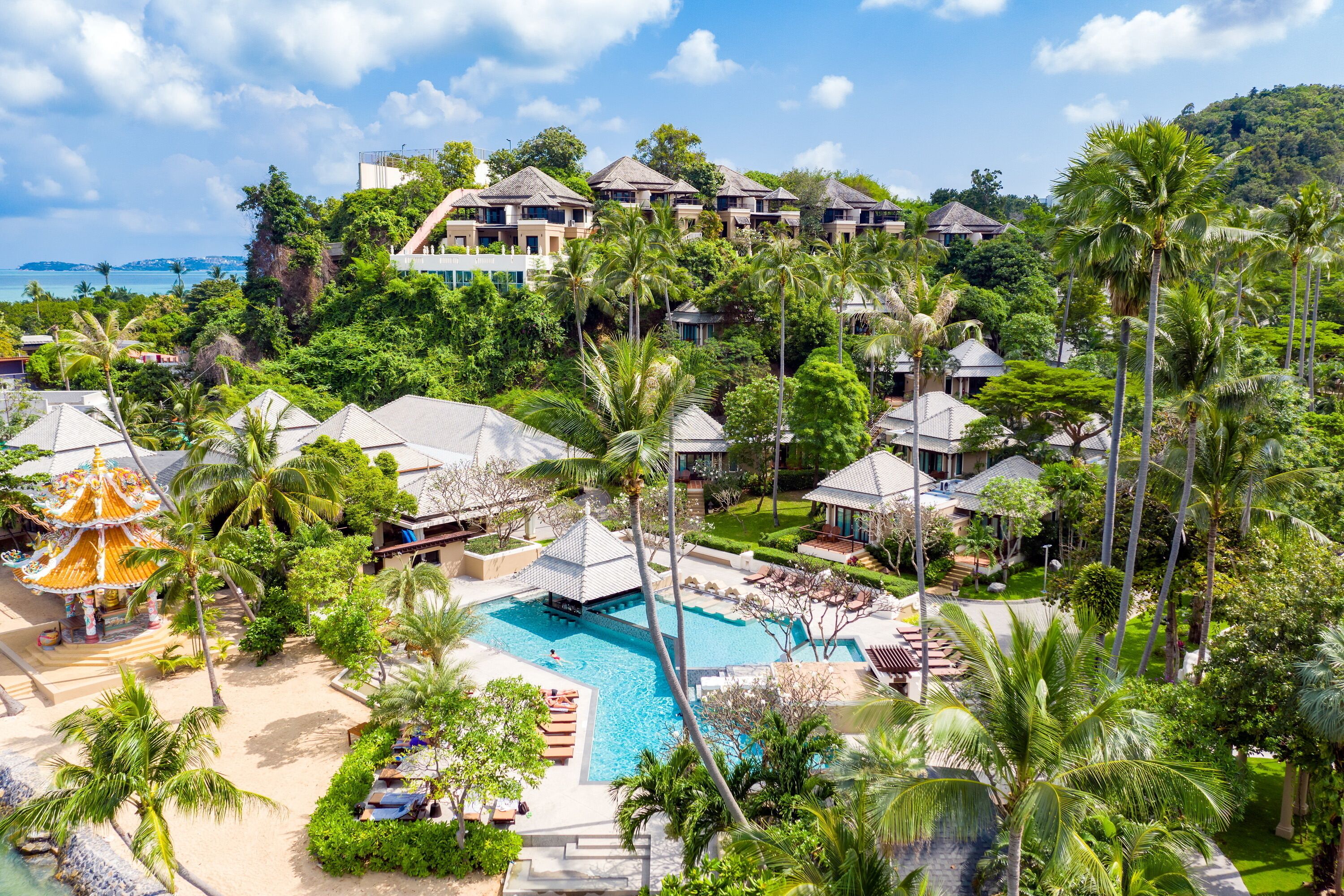 Un resort con varias construcciones tipo cabaña, una piscina central y exuberante vegetación tropical.