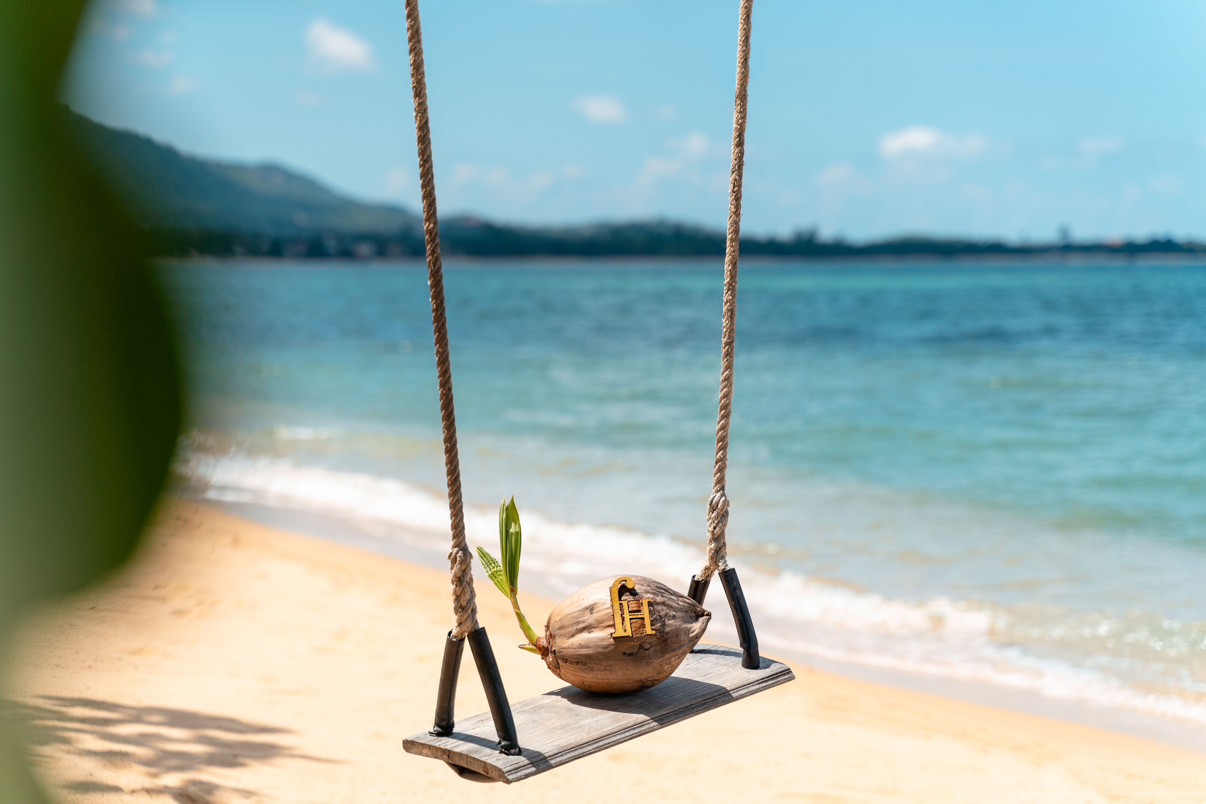 Una hamaca de madera con un coco y la letra 'H' en la playa.