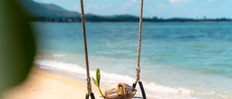 Una hamaca de madera con un coco y la letra 'H' en la playa.