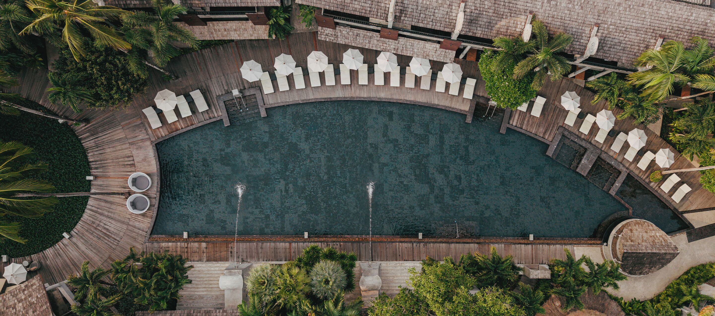 Vista aérea de un área de piscina con cubierta de madera, sillones de descanso y sombrillas.