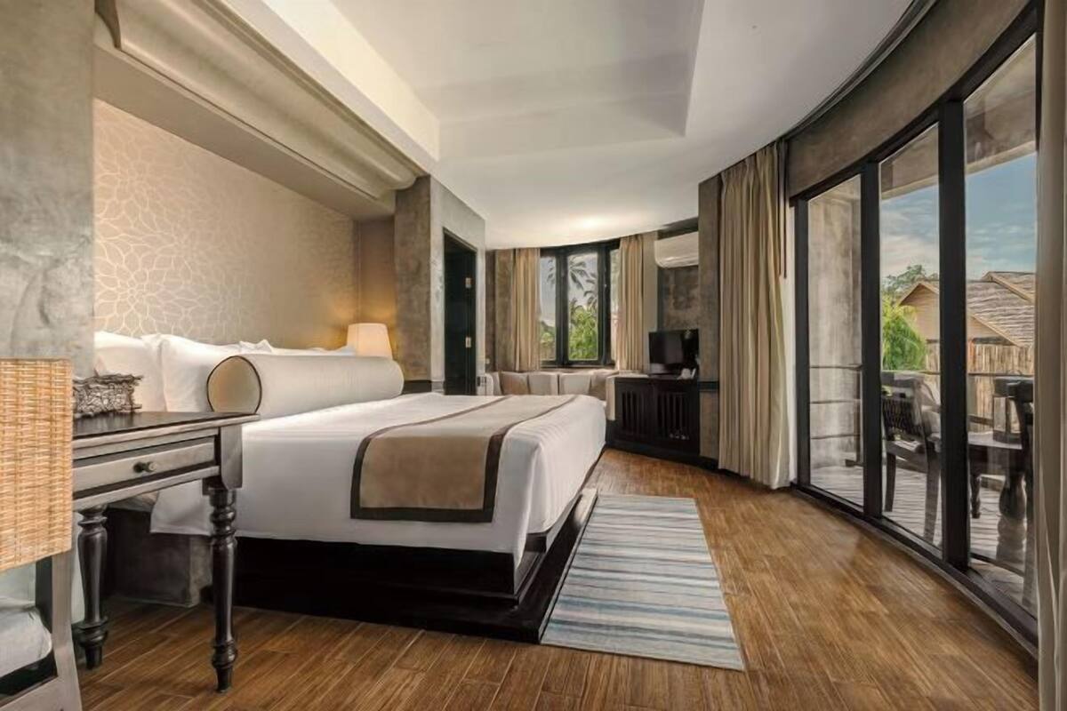 A hotel room with a large bed, a desk, a TV, and a sliding glass door to the outside.