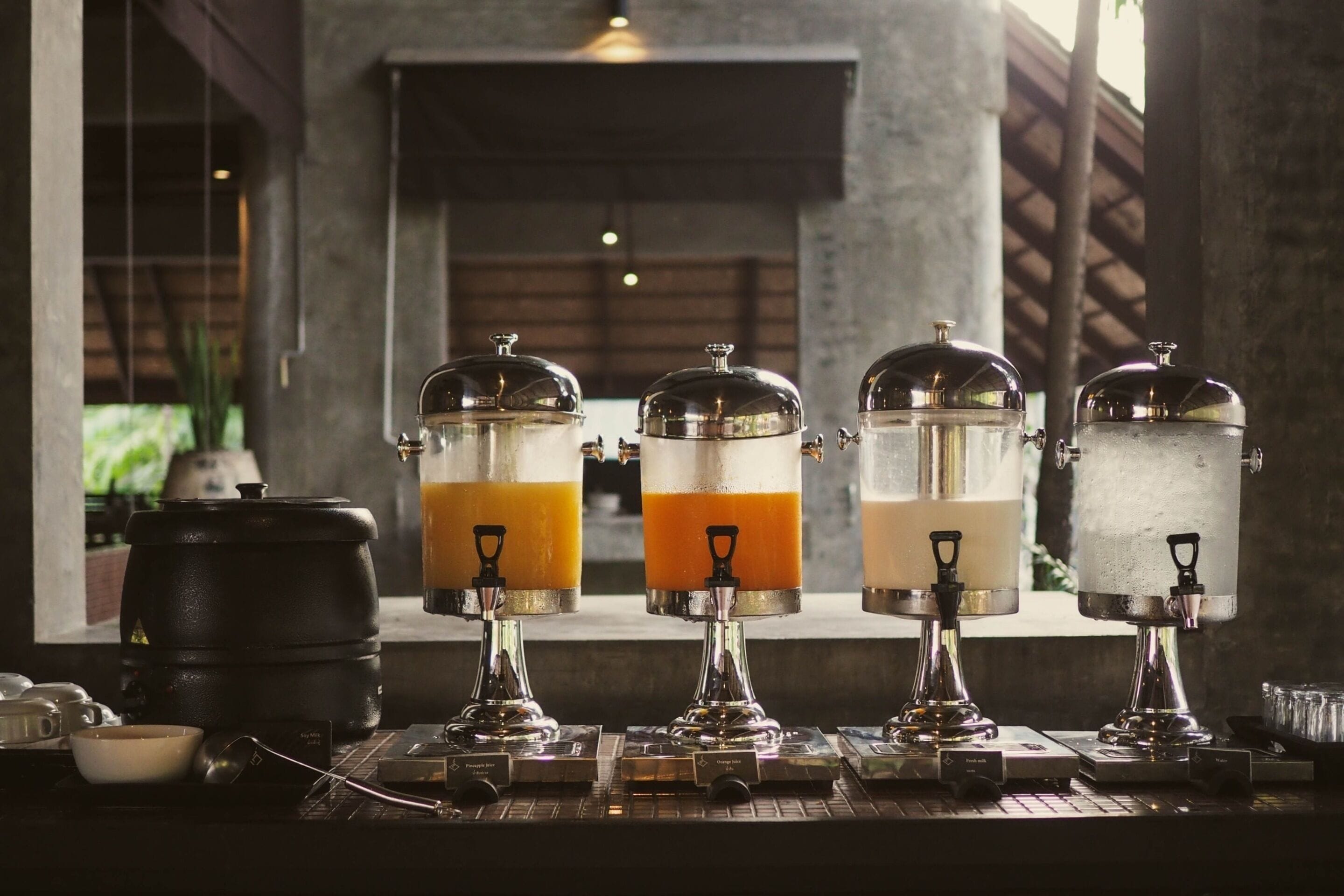 Fyra dryckesautomater med olika färgade vätskor, en kaffekvarn och en stor bryggkanna står på bardisken.