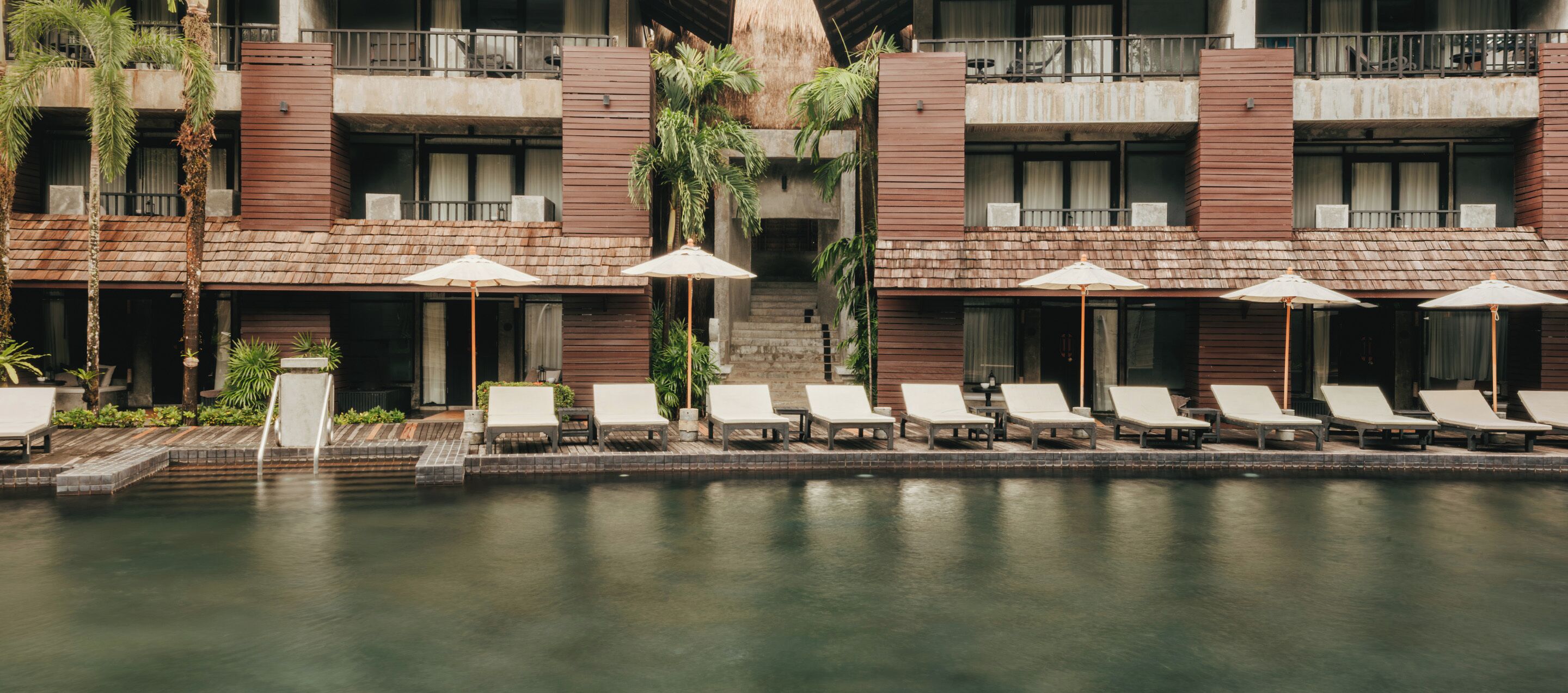 Ein Hotel mit Poolbereich, der Liegestühle und Sonnenschirme bietet, einer Treppe zu einem Balkon sowie einem modernen architektonischen Design.