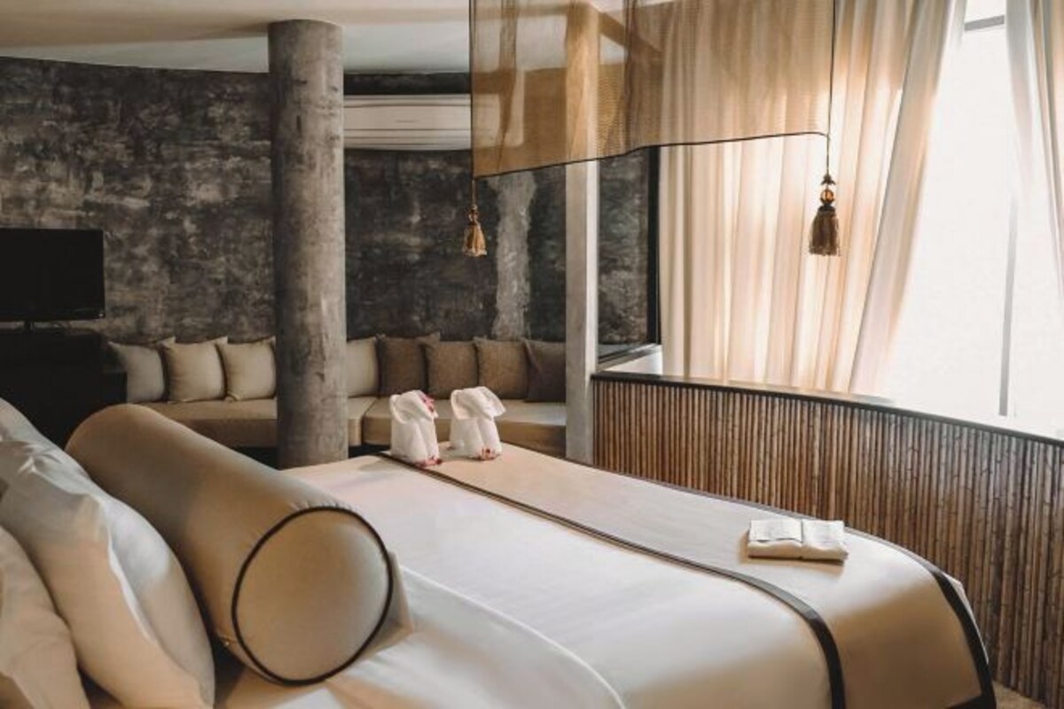 Una habitación de hotel moderna con una cama grande, una zona de estar, un televisor y un ventanal con cortinas.
