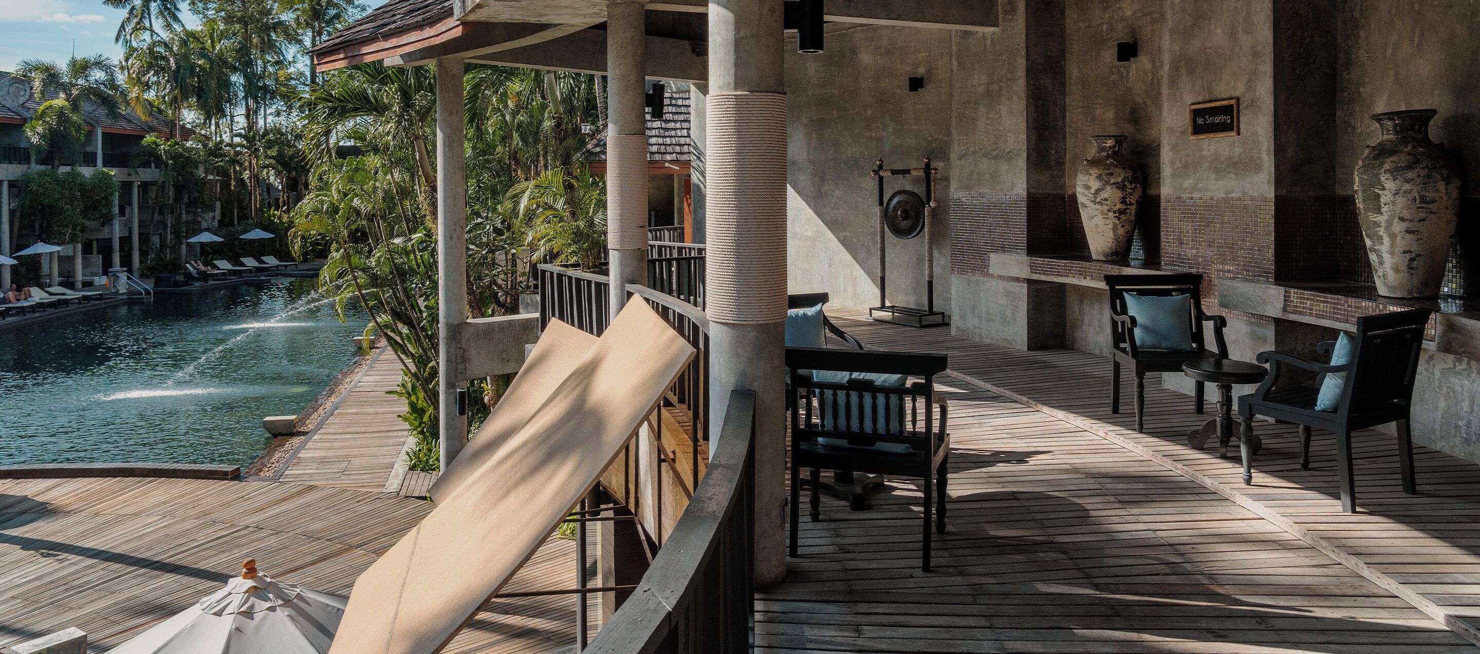 A wooden deck with a pool, lounge chairs, and a stone wall with a vase.