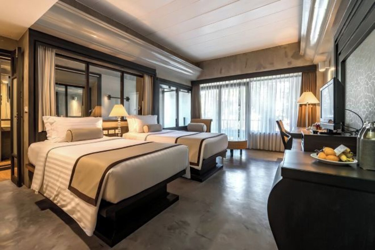 Una habitación de hotel moderna con dos camas, un escritorio y un ventanal grande.
