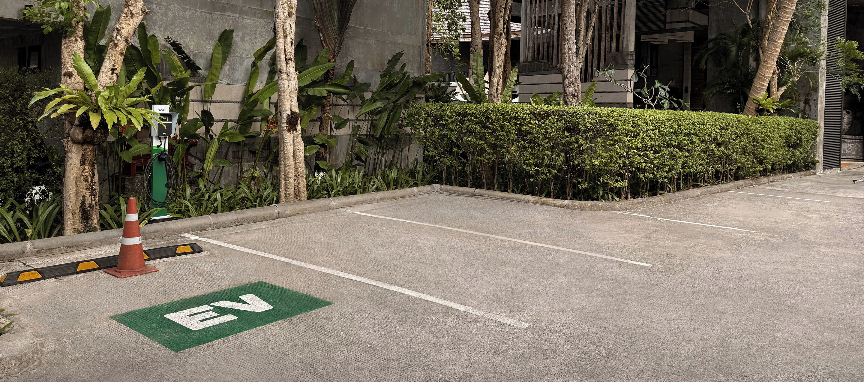 A parking area with EV charging stations, a clear path, and a hedge.