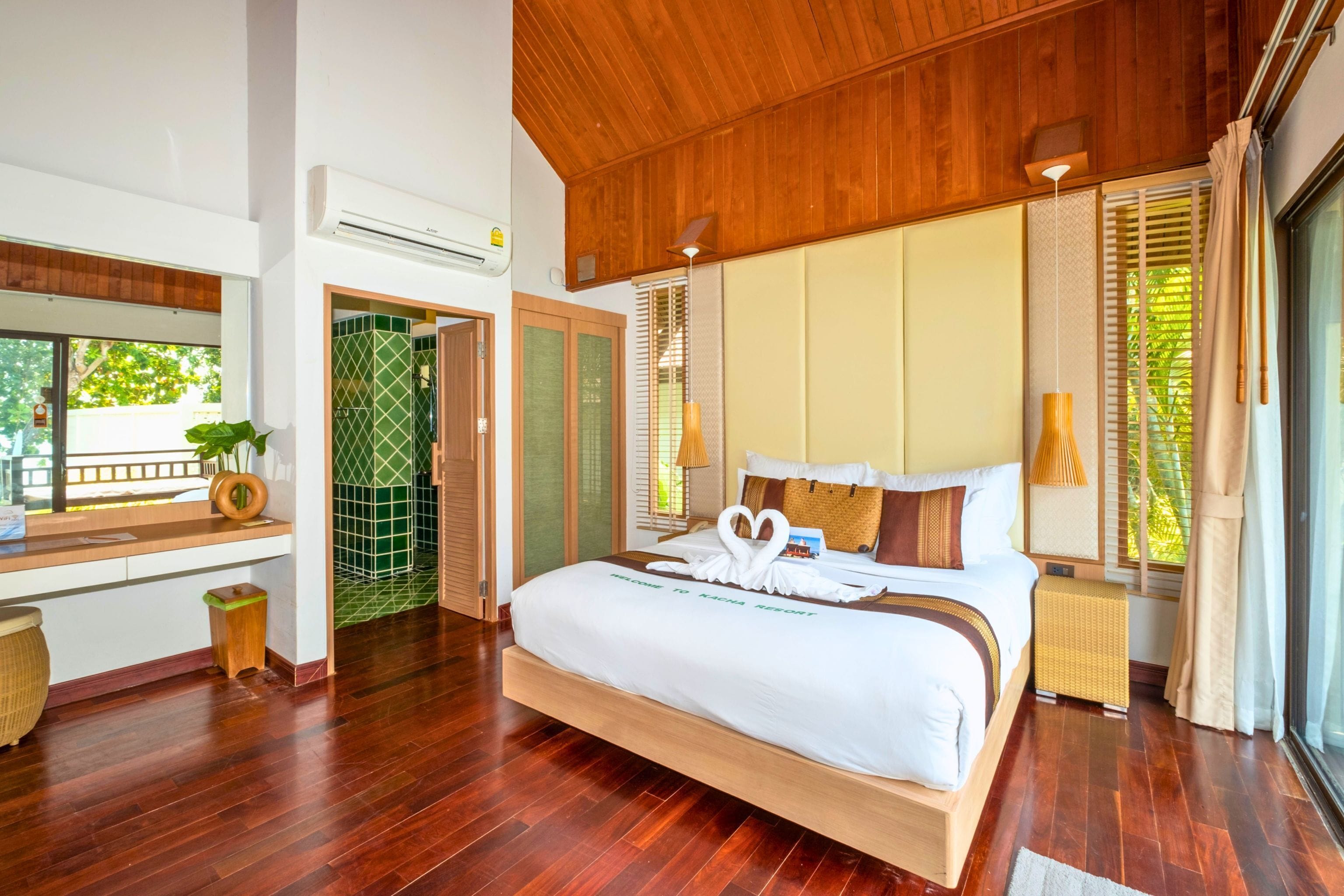 Een ruime slaapkamer met een groot bed, houten vloeren, een inbouwkruk en uitzicht op groen.
