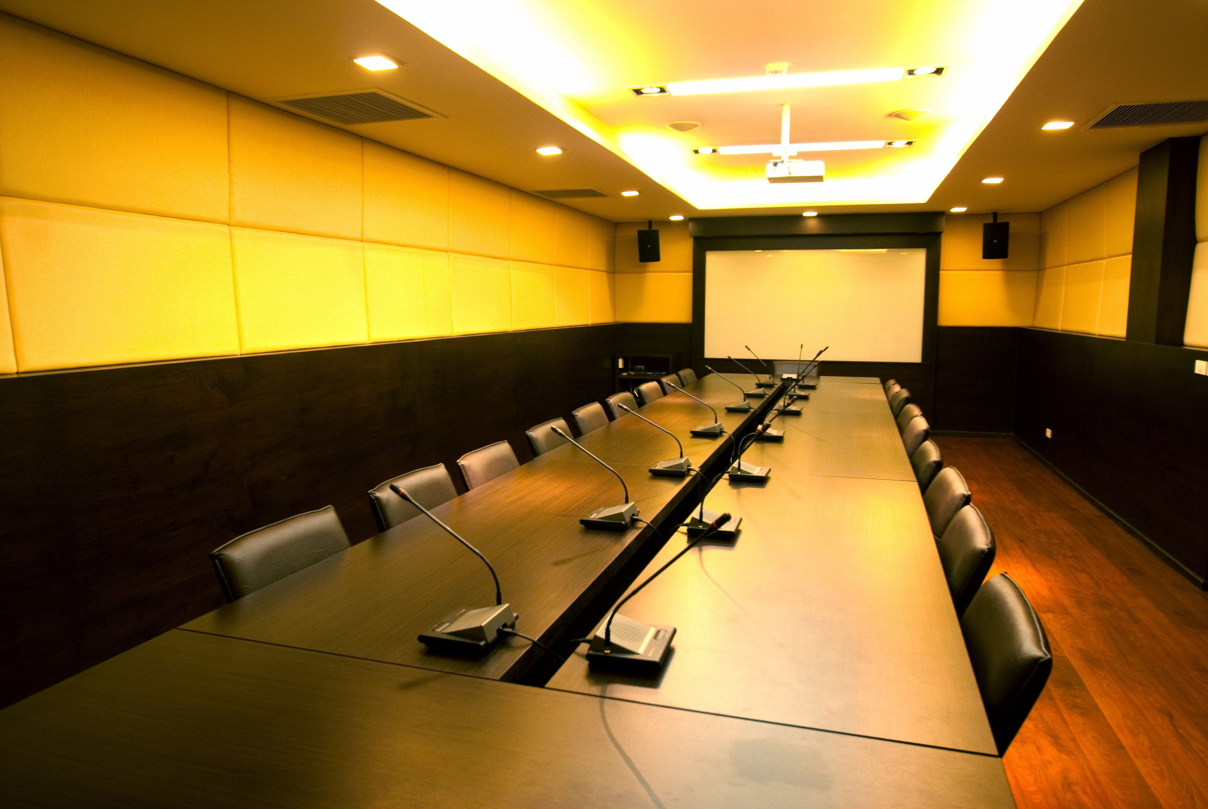 Un salón de conferencias con una mesa larga, varias sillas y una pantalla para proyector.