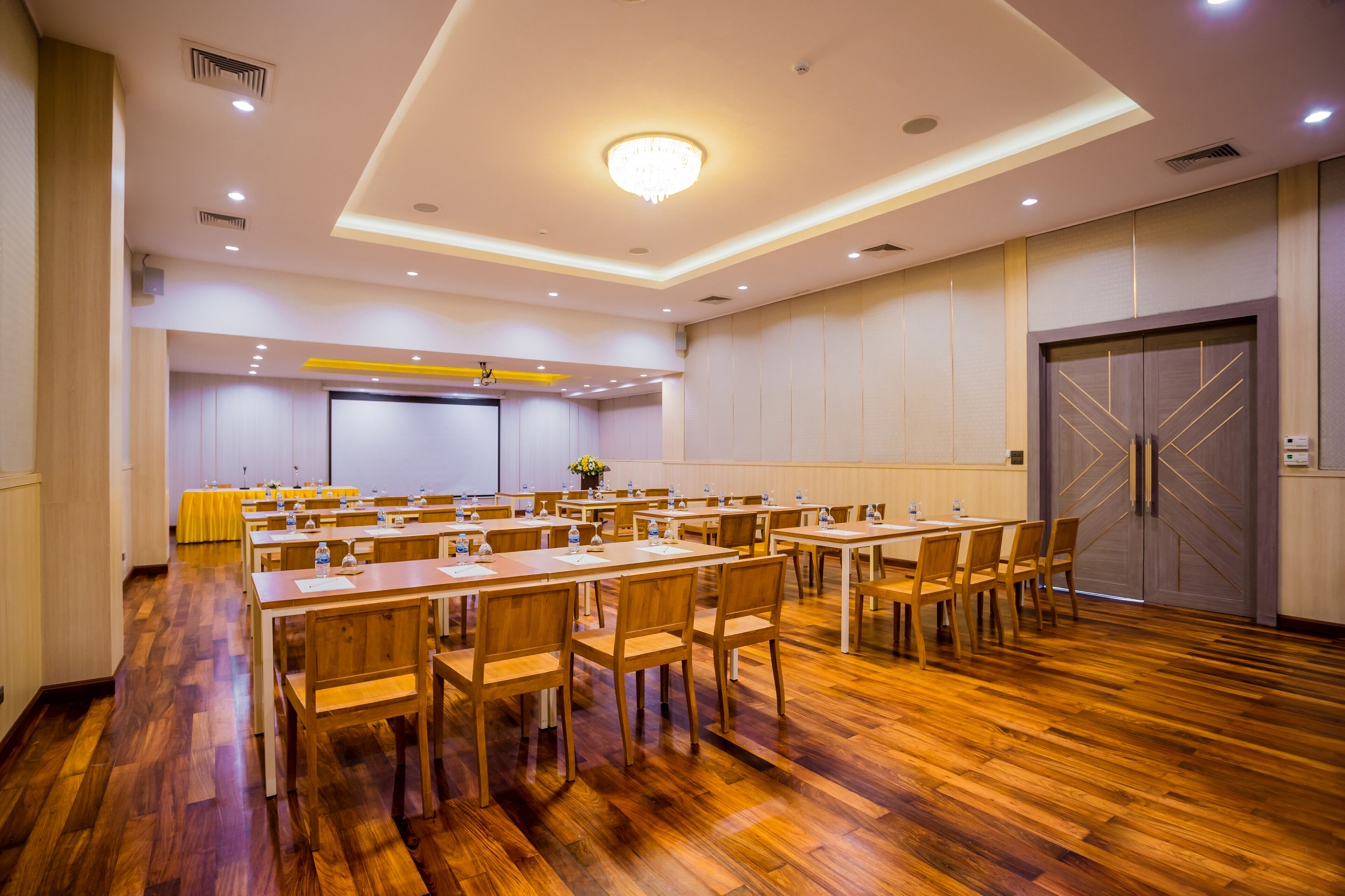 Una sala conferenze con diversi tavoli e sedie, un grande schermo e una porta con un motivo geometrico.