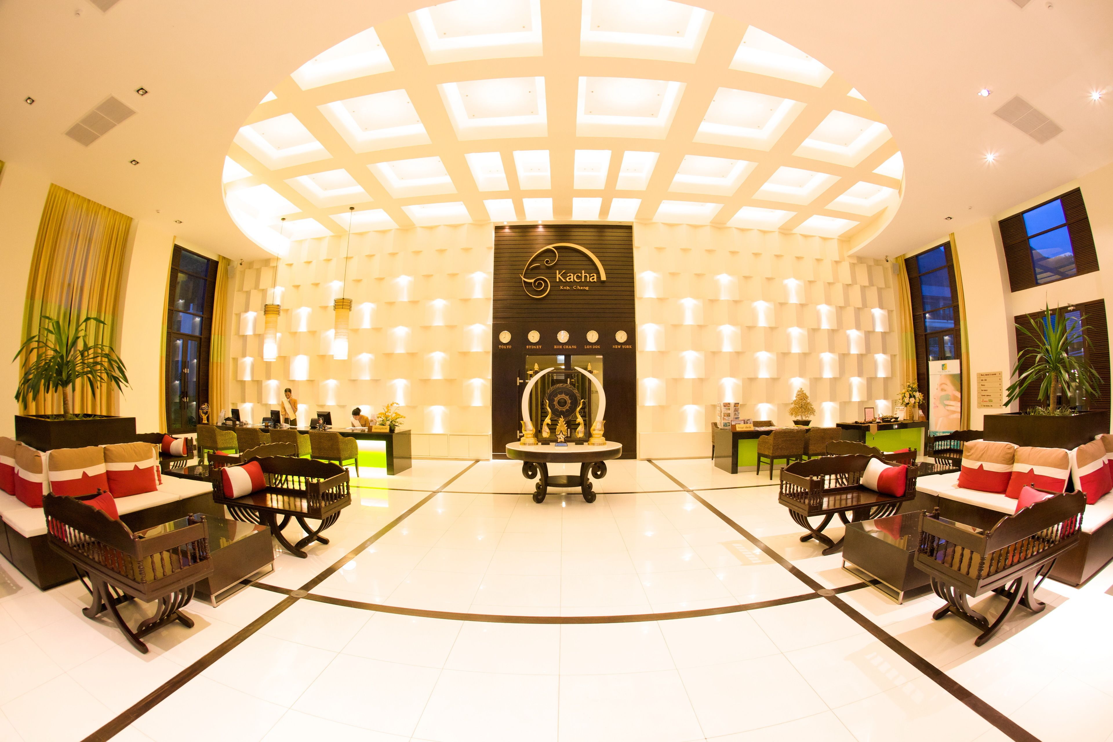 Un hall de hotel con un mostrador de recepción central, zonas de estar y una pared decorativa con iluminación.