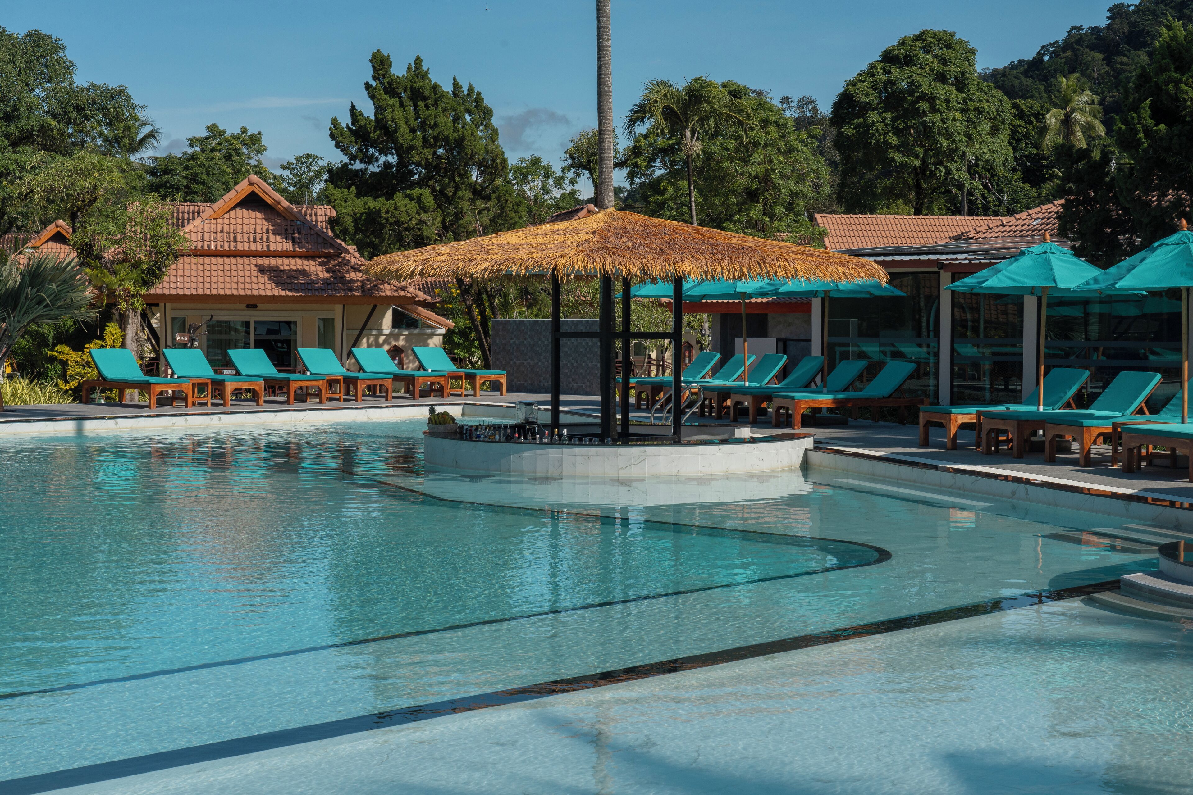 Un espace piscine doté de chaises longues et de parasols, entouré de bâtiments aux toits recouverts de tuiles.