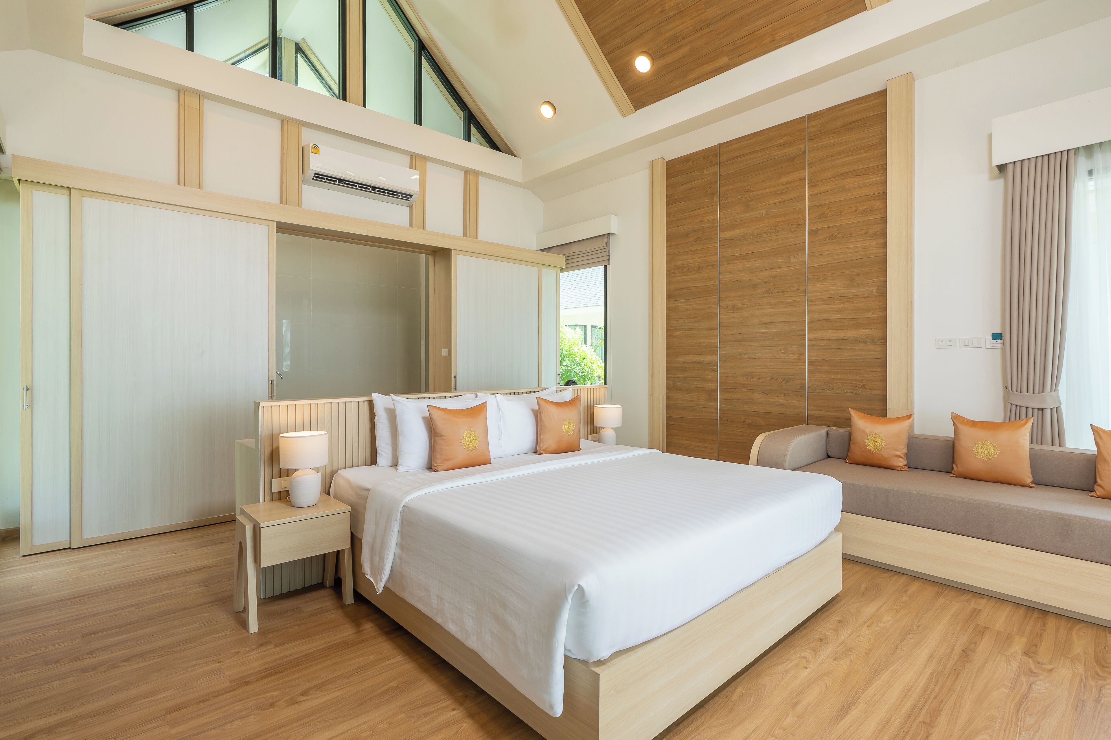 A modern hotel room with a large bed, built-in wardrobe, and a seating area with cushions.