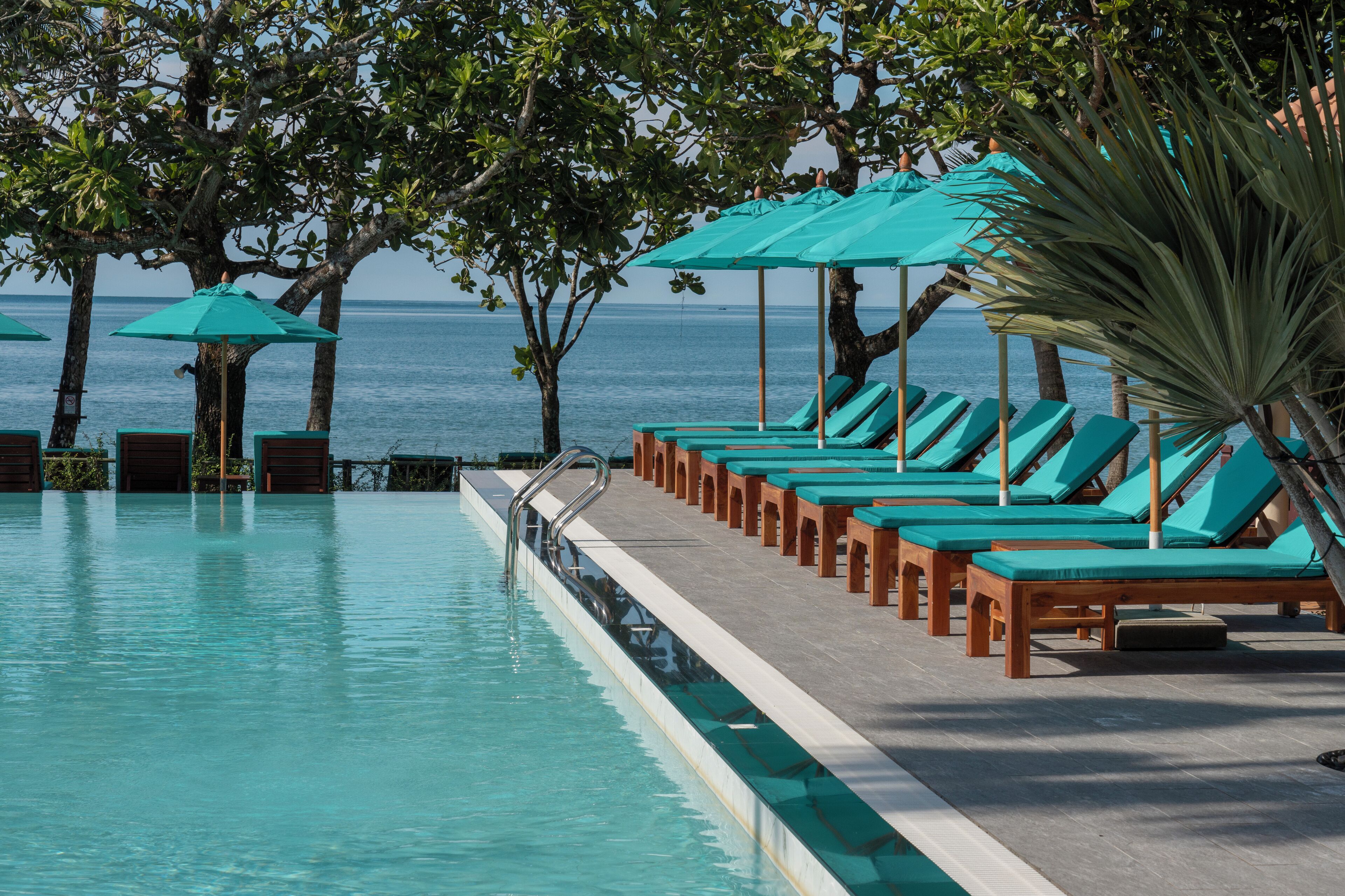Un espace aménagé au bord de la piscine, avec des chaises longues et des parasols, une vue dégagée sur la mer et une piscine aux eaux calmes.
