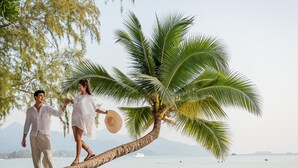 Ett par promenerar på en strand med en palmtree och en båt i bakgrunden.