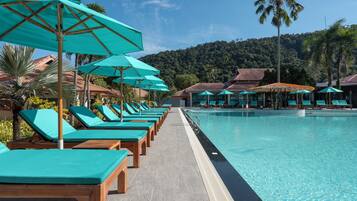 A poolside area with lounge chairs and umbrellas, a clear pool, and a mountainous backdrop.