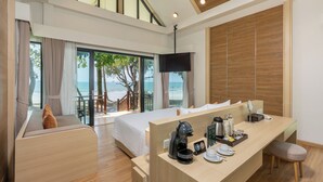 Ett modernt hotellrum med en säng, ett skrivbord med kaffebryggare och utsikt över stranden.