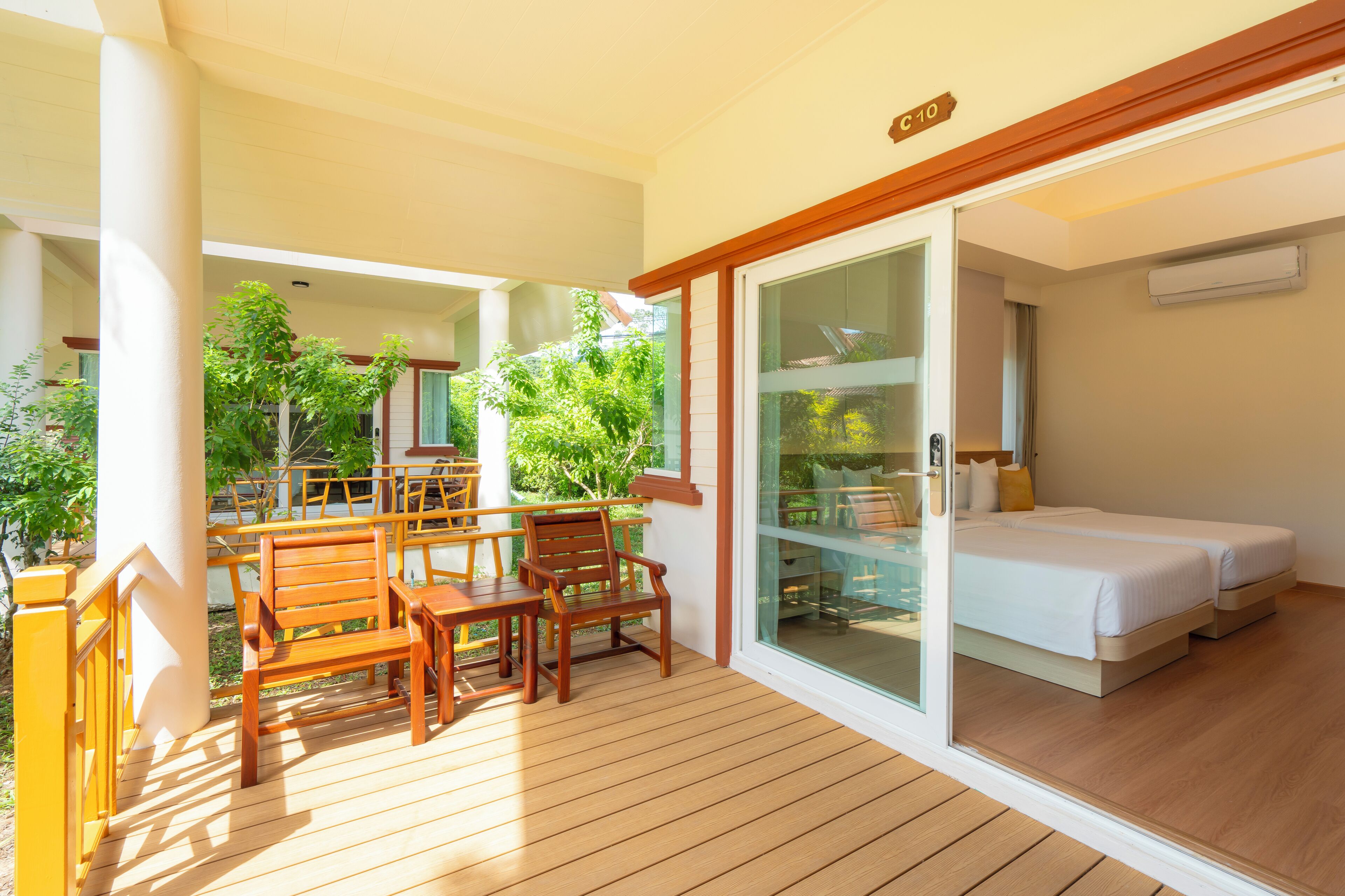 Una habitación con terraza de madera, puerta de cristal que da a un balcón y cama con dos almohadas.