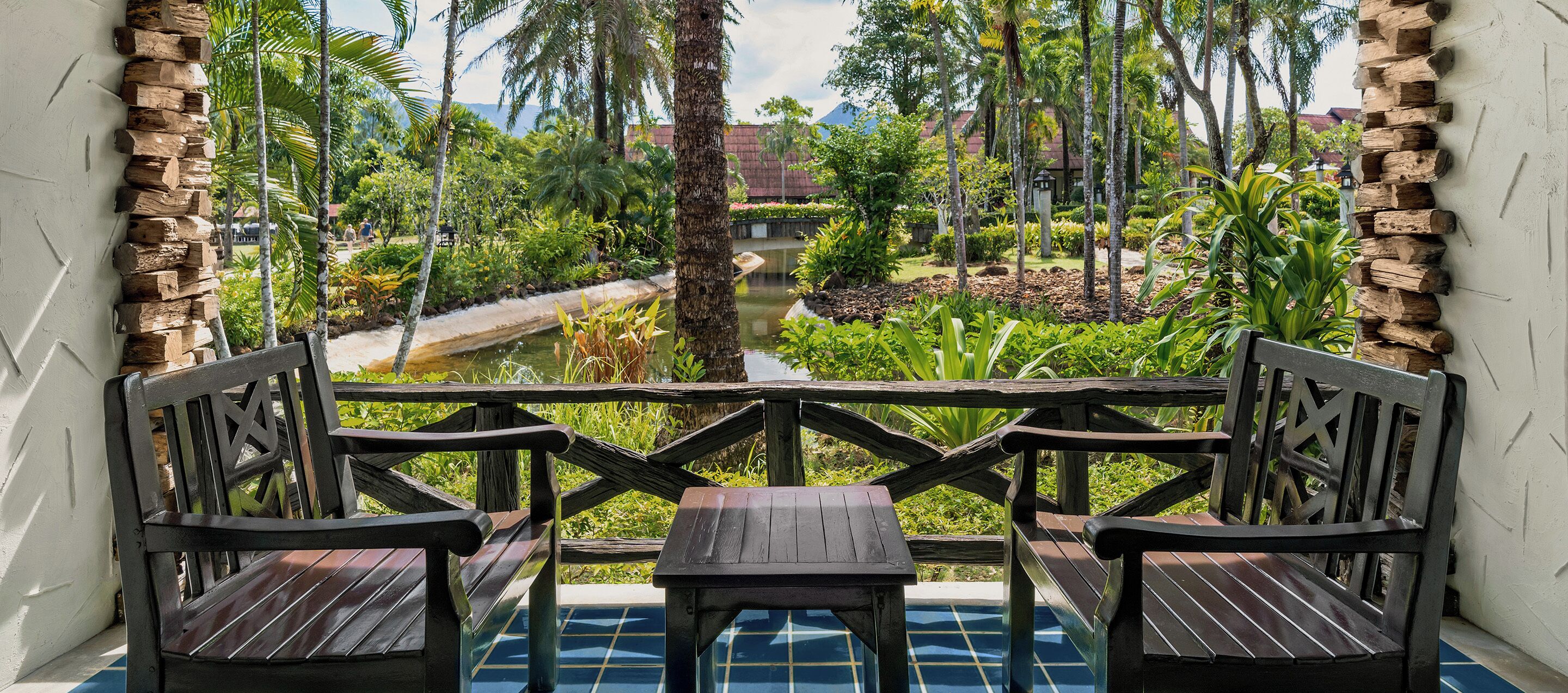 Un conjunto de banco y mesa de madera frente a una pared de piedra, con vistas a un exuberante jardín y un estanque.