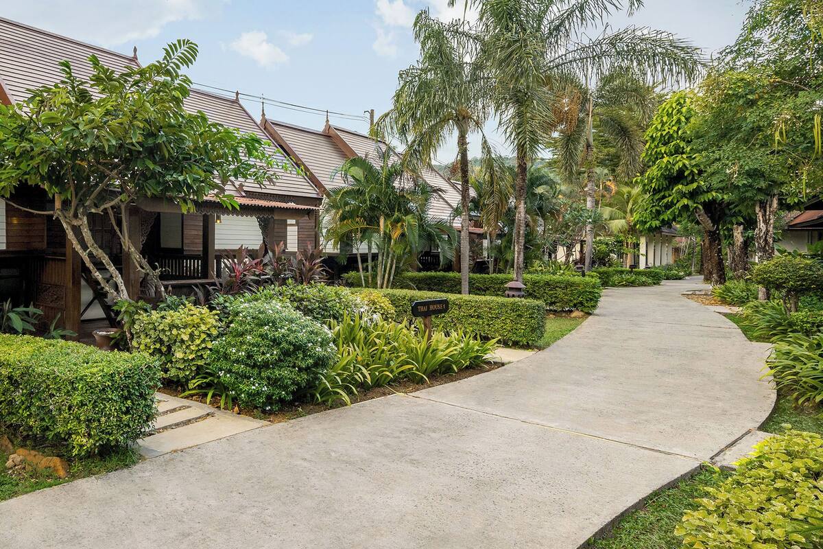 A pathway leading to a row of traditional-style buildings with a well-maintained garden and tropical plants.