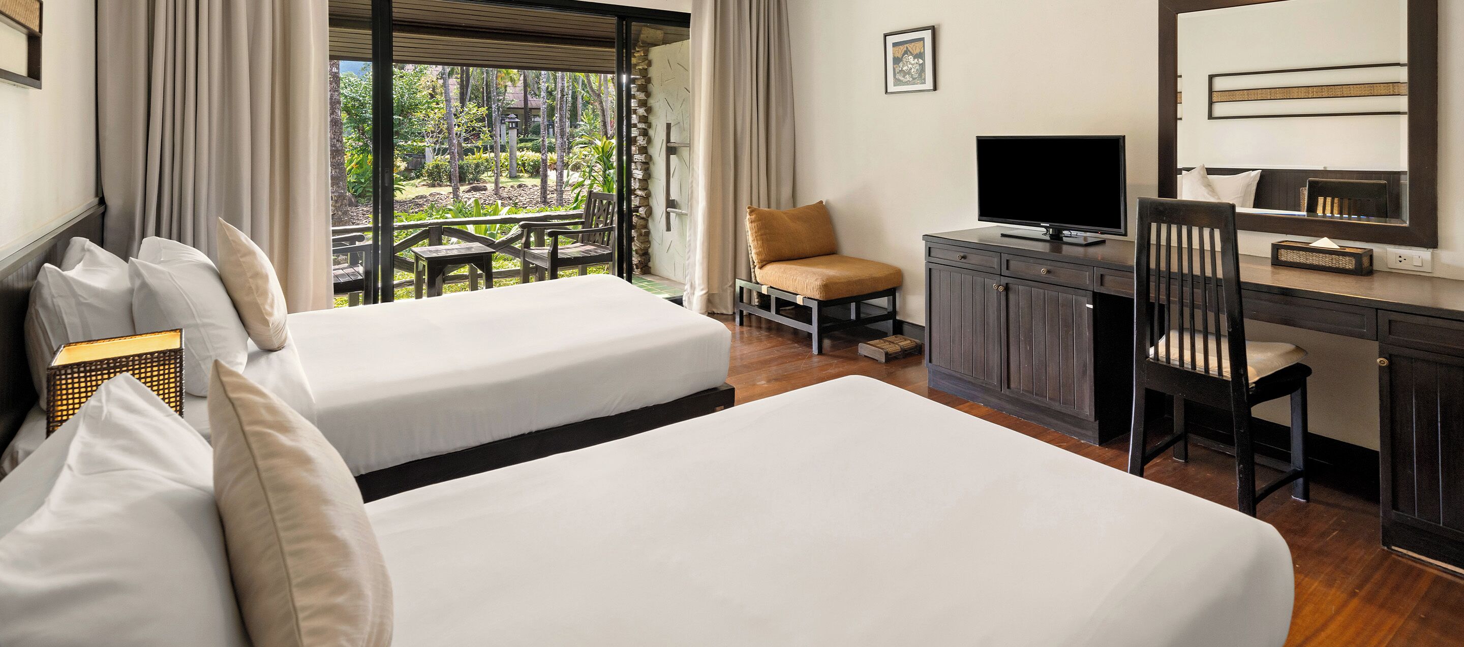Habitación de hotel con dos camas, un escritorio con televisor, una silla y vistas a un jardín a través de amplios ventanales.