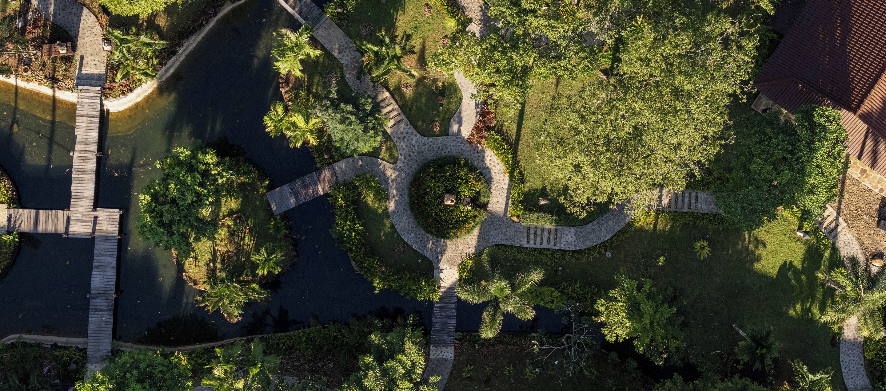 Vista aérea de una zona ajardinada con un jardín circular central, rodeado de senderos y bordeado por árboles y arbustos.